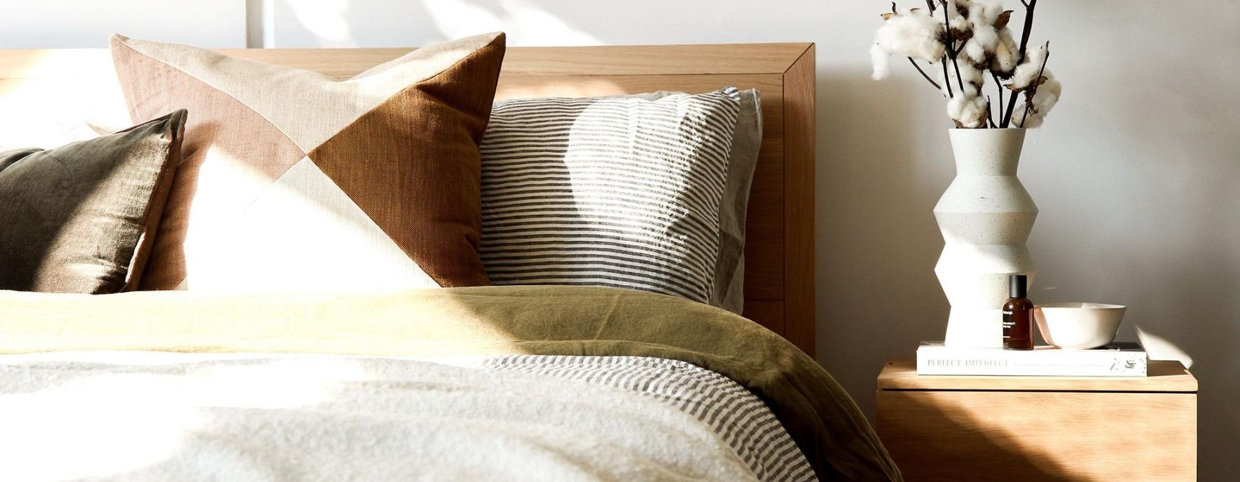 swath of sunlight shines across a well made bed and bedside table with a vase of cotton plants